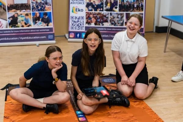 Three girls in safety goggles programming a drone on the mission mat with a tablet during a STEMdrones workshop