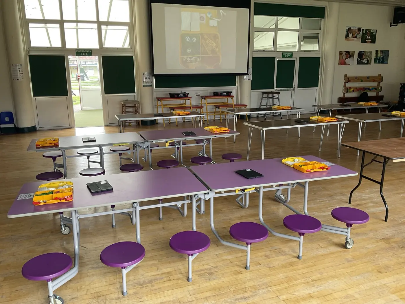 A school hall set up for Beginner STEMbotics, with mobile dining tables arranged around the perimeter and robotics kits ready for students