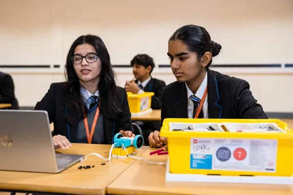 Two girls coding and building a SPIKE Prime wheeled robot with colour sensor at their desk