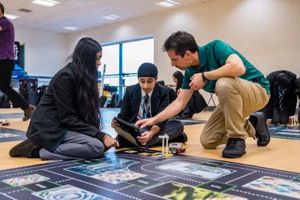 Instructor guiding students testing an autonomous vehicle robot on a road mat with AI-powered navigation