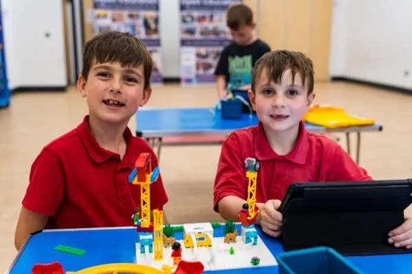 Two boys proudly displaying their completed LEGO SPIKE Essential robot build with tablet coding interface