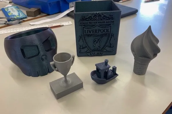 Display of finished 3D printed student designs including trophies, planters, and custom models