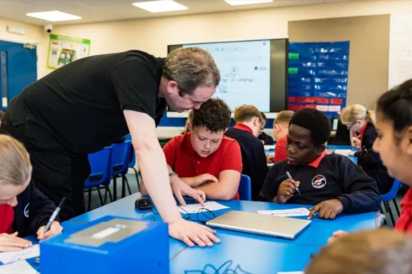 Instructor helping students with cryptography code-breaking challenges during a Cybersecurity workshop