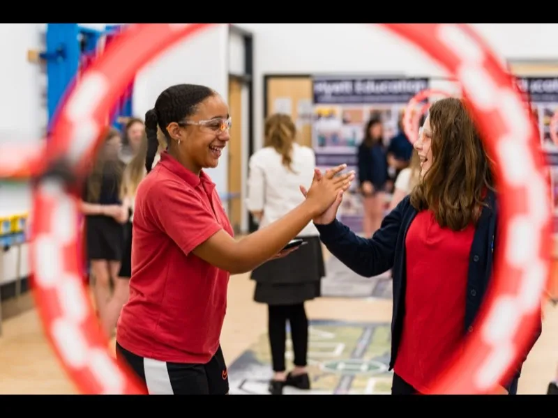 Two girls celebrating with a high-five through a drone racing hoop