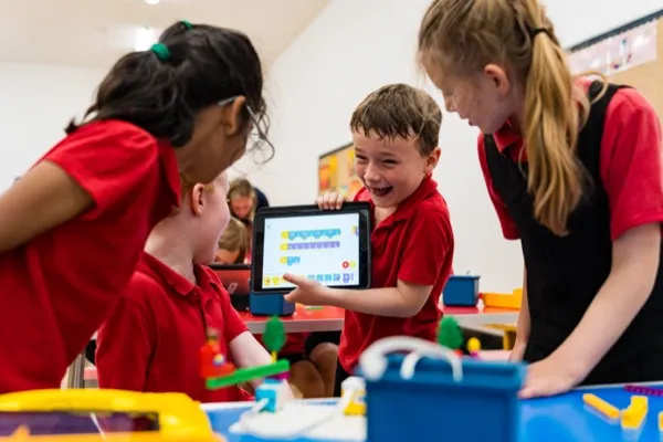 Children excitedly showing their SPIKE robot programming on an iPad with LEGO builds on the table