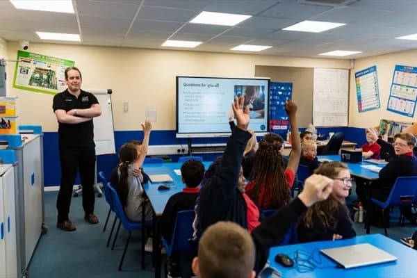 Instructor presenting cybersecurity challenges on screen with students raising their hands