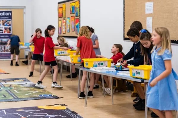 Wide view of a school hall with children at tables building robots with SPIKE kits and mission mats on the floor