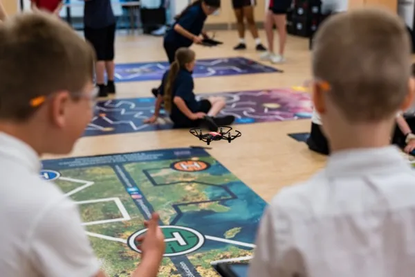 A drone in flight over the mission mat as students watch during a STEM drones workshop