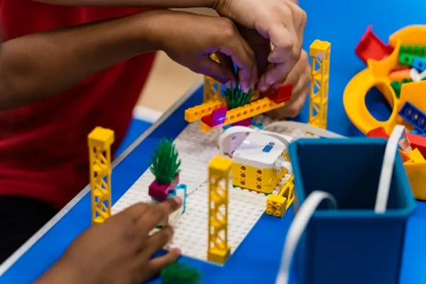 Hands building a LEGO SPIKE fairground model on a baseplate during a robotics workshop