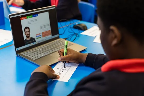 A student writing cipher code at a desk with the encryption app visible on a laptop screen