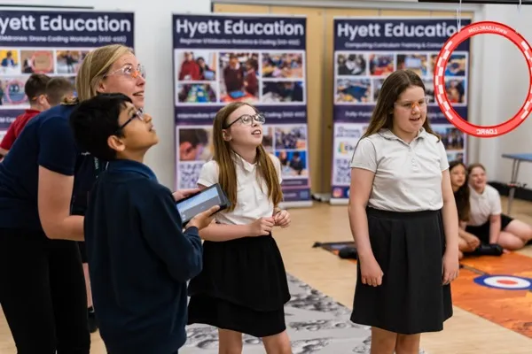 Students watching a drone fly through a hoop obstacle during a coding drones workshop