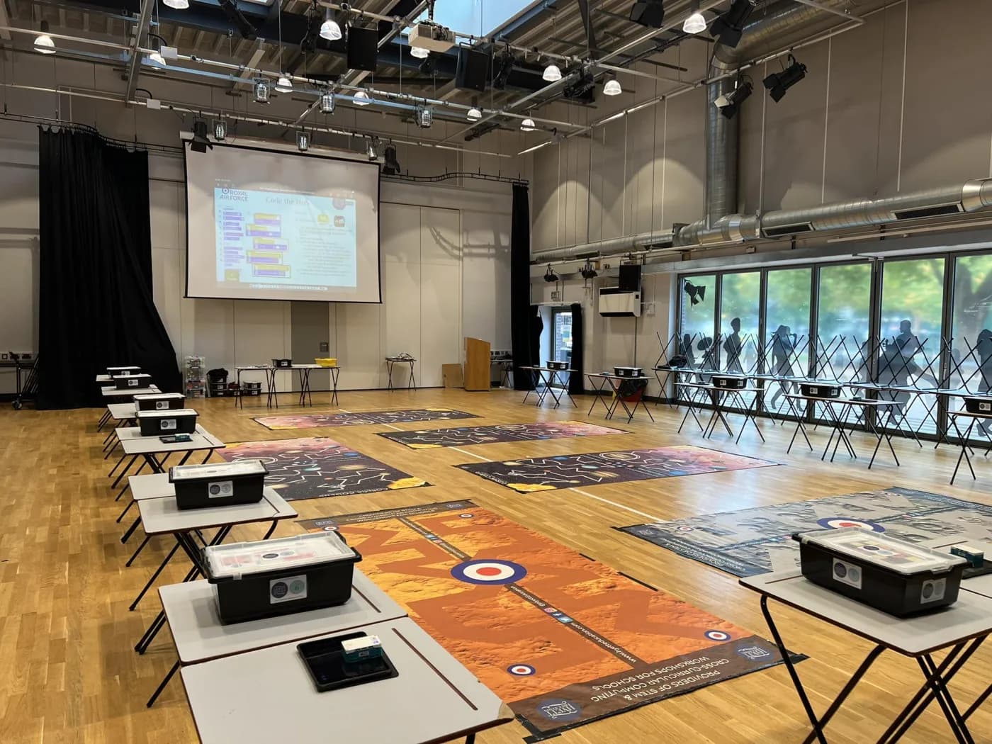 School hall set up for an Intermediate STEMbotics workshop with exam tables paired for each team in a U-shape and challenge mats in the centre