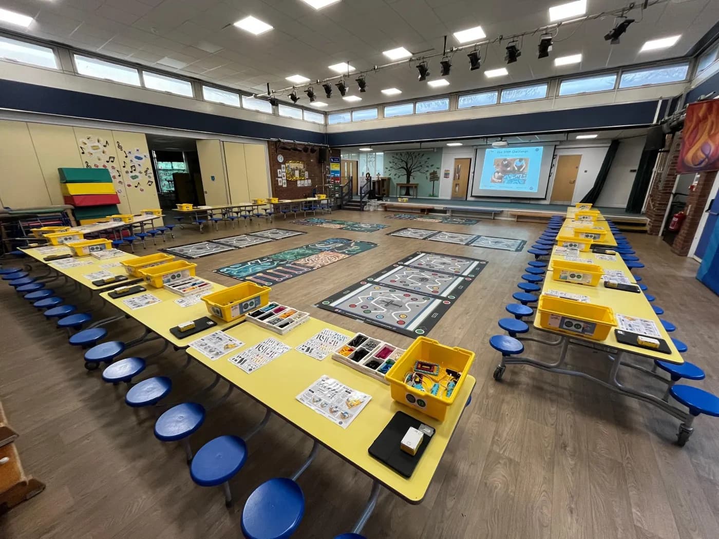 School hall set up with mobile dining tables in a U-shape and space in the centre for coding challenge mats