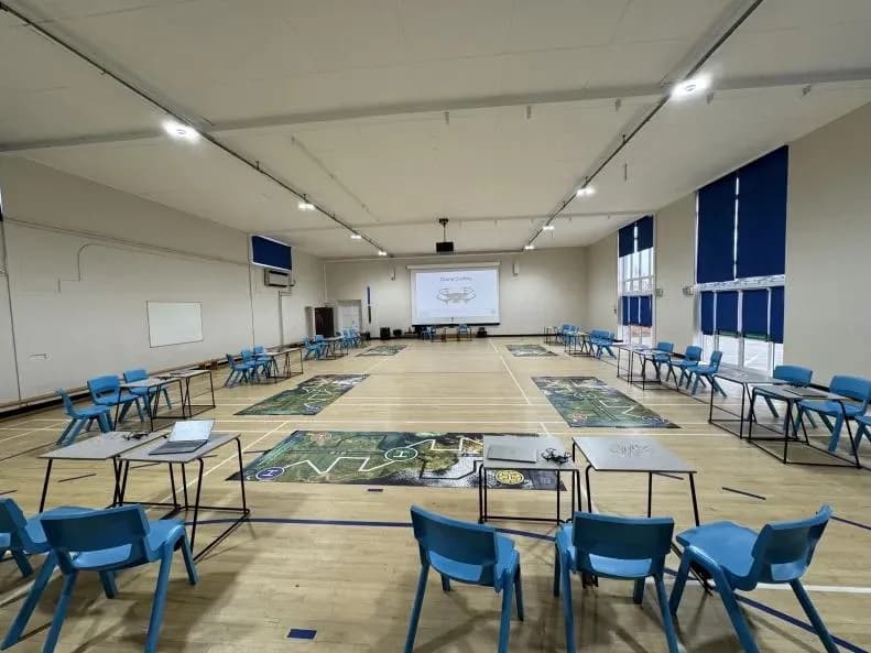 Large school hall set up for a Drone Coding workshop with paired exam tables spaced around the perimeter and challenge mats across the floor